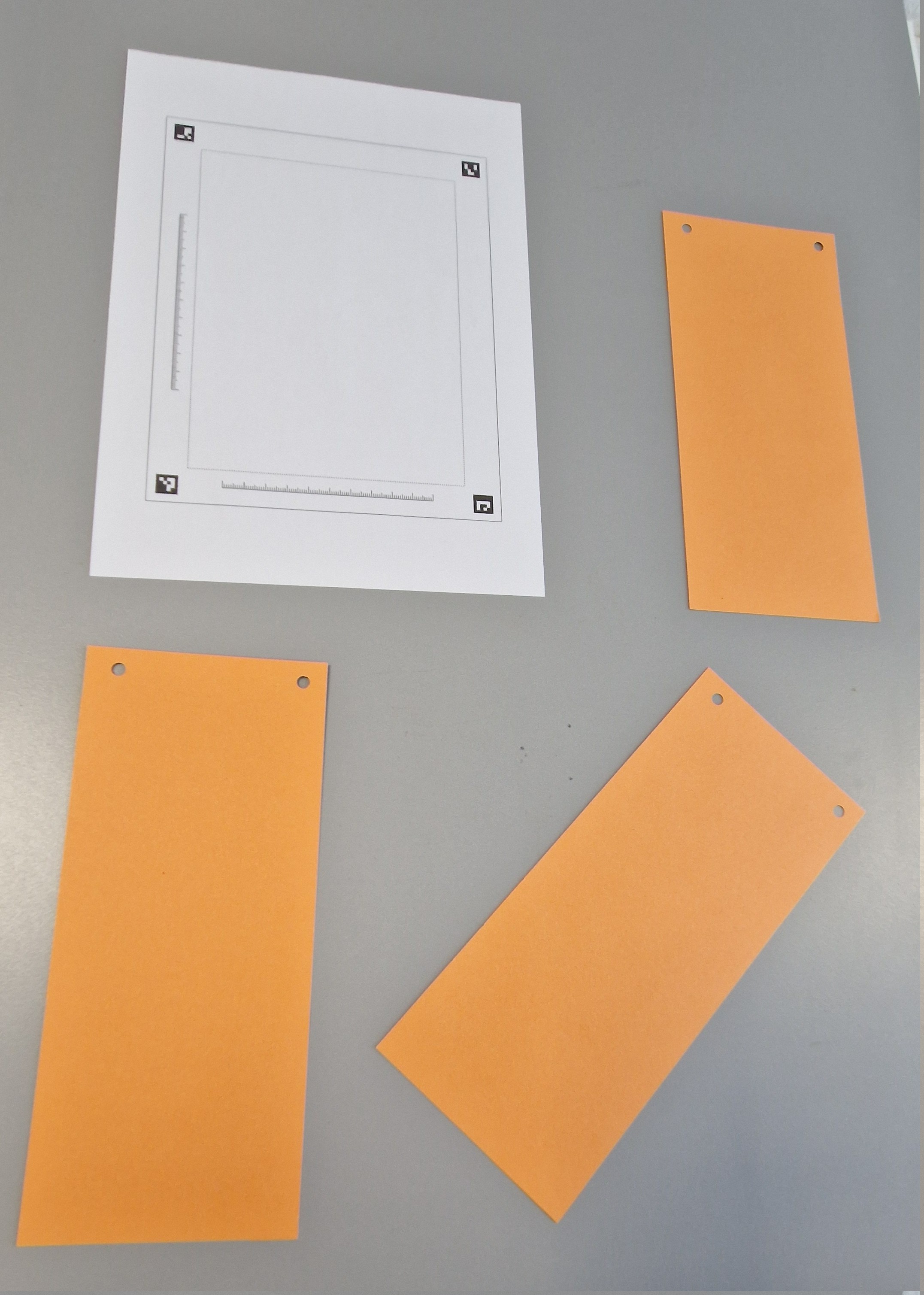 Rohfoto (perspektivisch): Markerrahmen als DIN-A4-Blatt (oben rechts) und Prüfobjekte auf einer Ebene